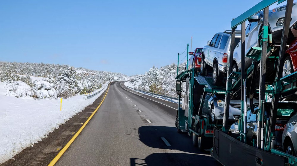 Car carrier trailer transporting multiple vehicles on a snowy highway, showcasing auto transport services in winter conditions.