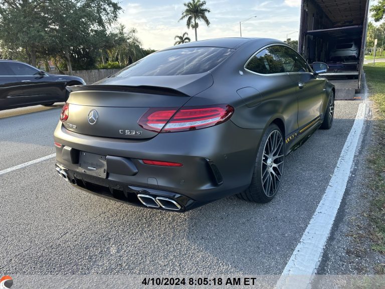 Matte black Mercedes-Benz C63 AMG parked roadside, preparing for enclosed auto transport with luxury car hauler in the background